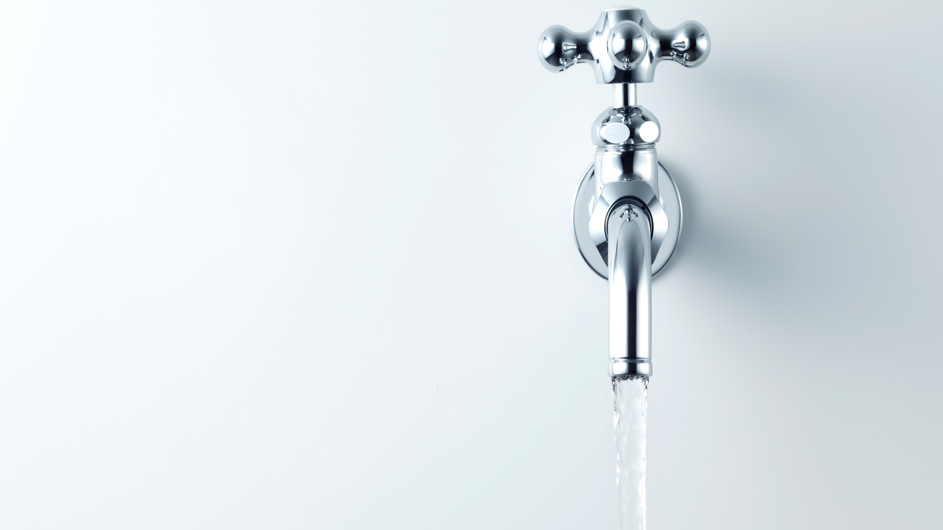 Minimalist image of a shiny chrome wall-mounted faucet with water flowing, set against a smooth white background