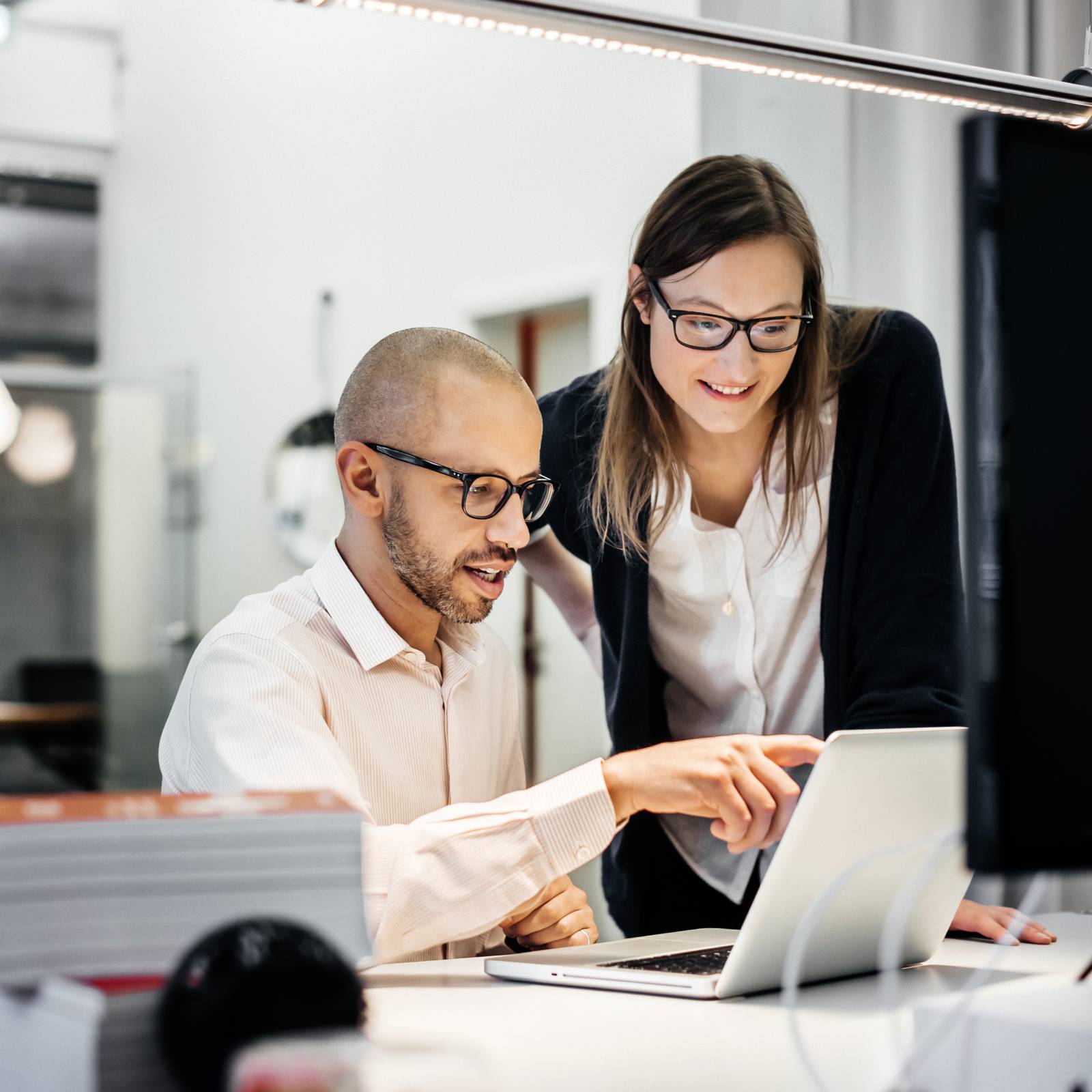 Two work colleagues discuss something on a laptop screen at a desk