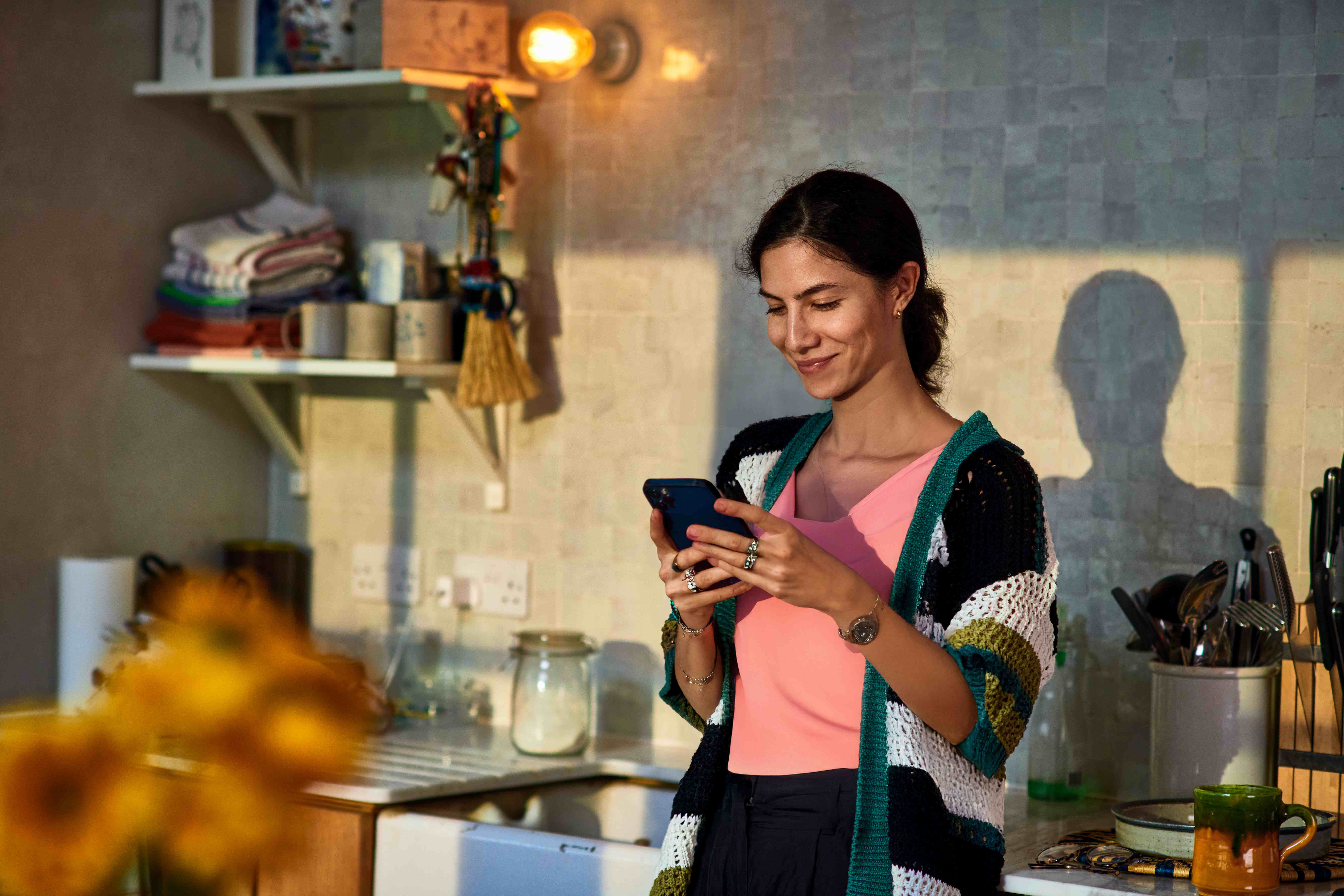 A lady leans against her kitchen sink while using her smartphone