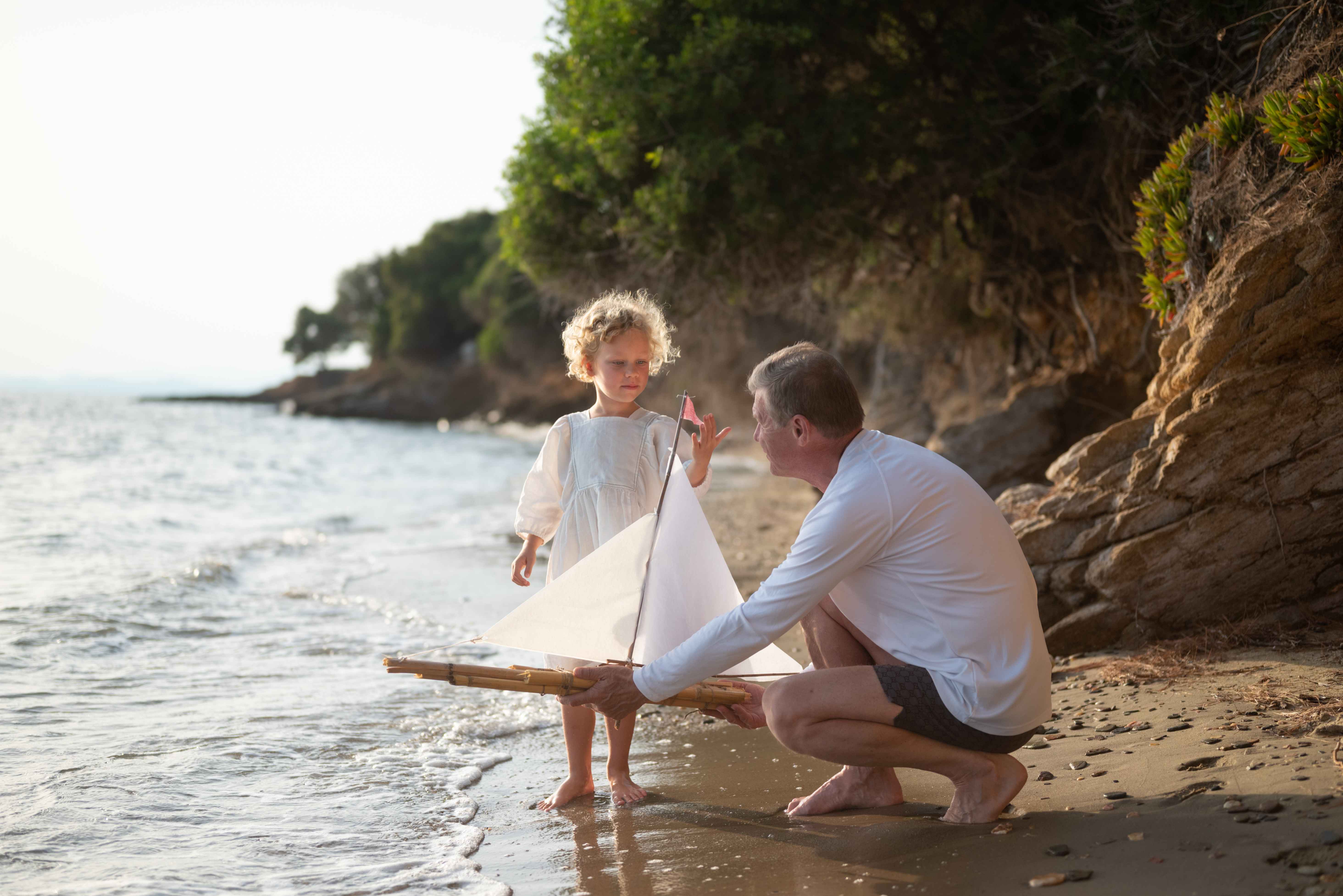 Father and daughter pushing toy boat into the ocean