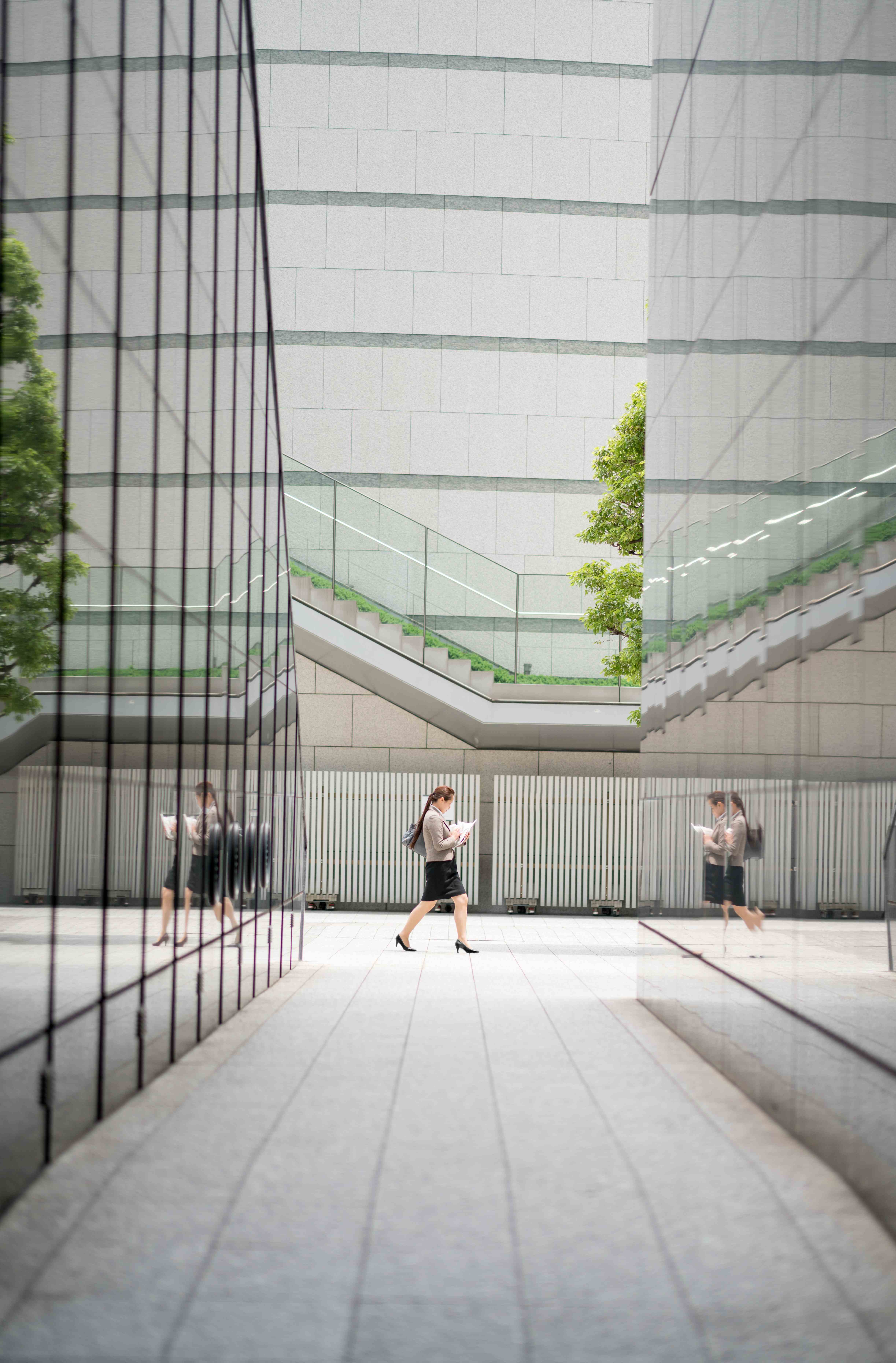 An office worker walks between buildings in the city, their figure reflected on the glass of the buildings around them