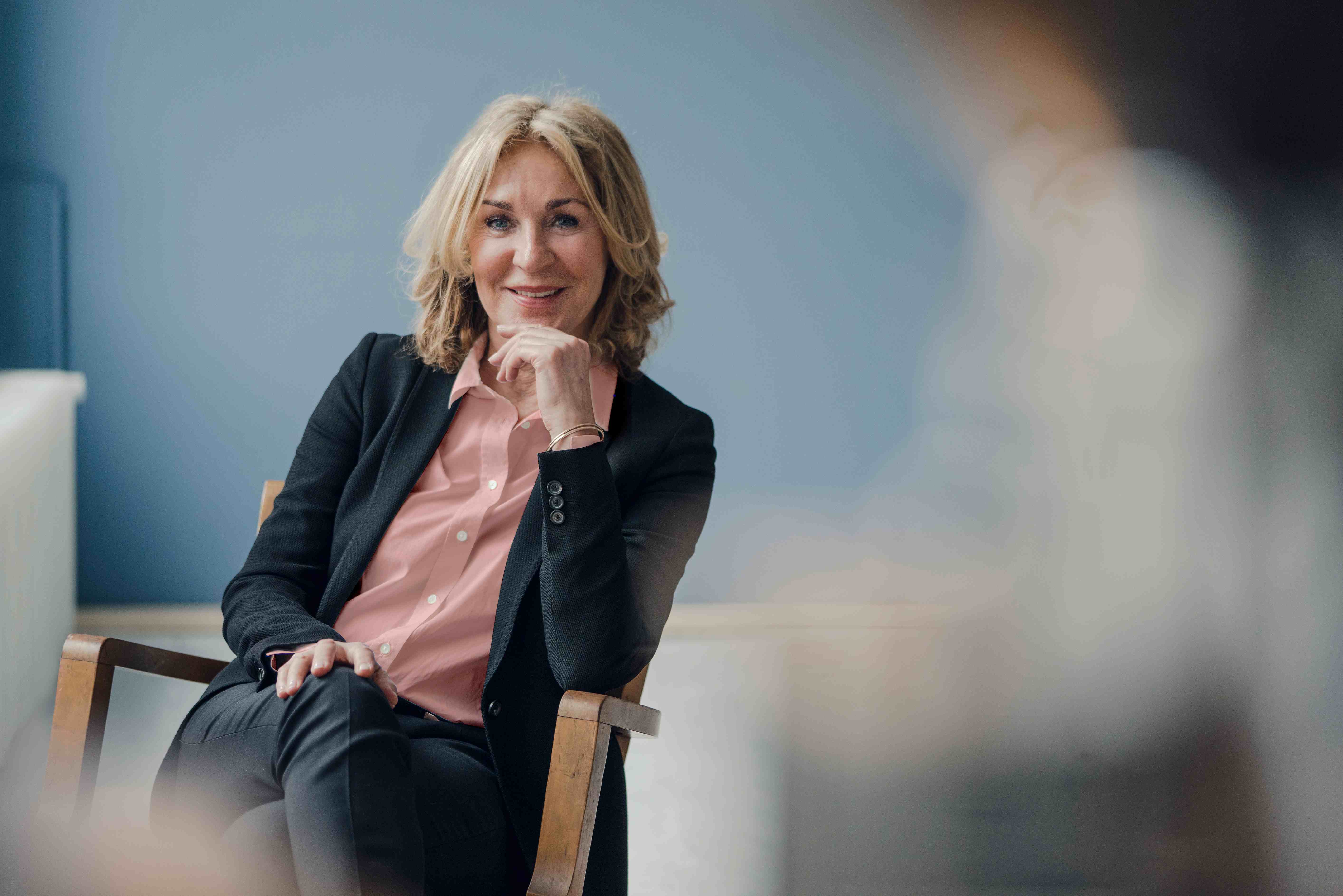 A professional woman looks towards the camera with a curious facial expression while sat in a chair