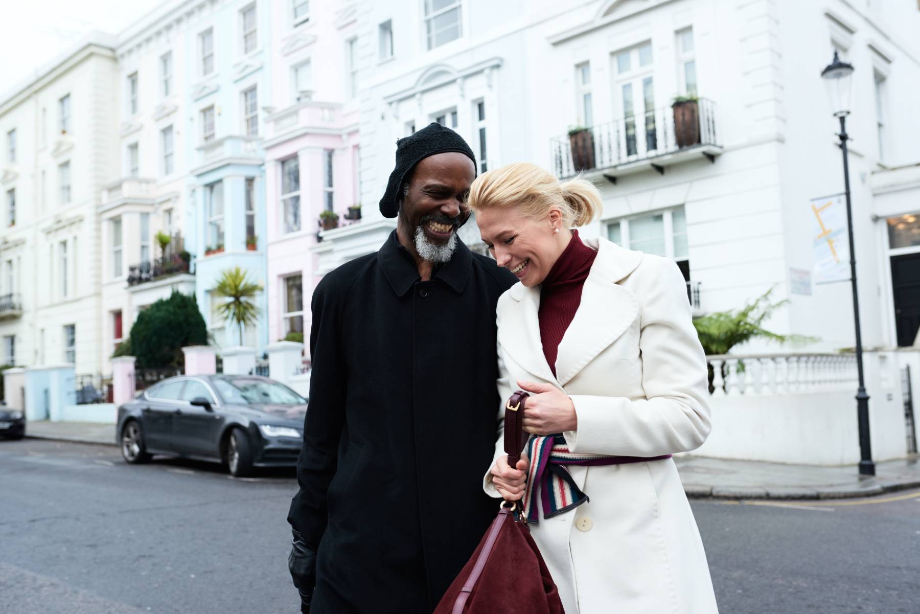 A couple laugh together while walking along a terrace housed street