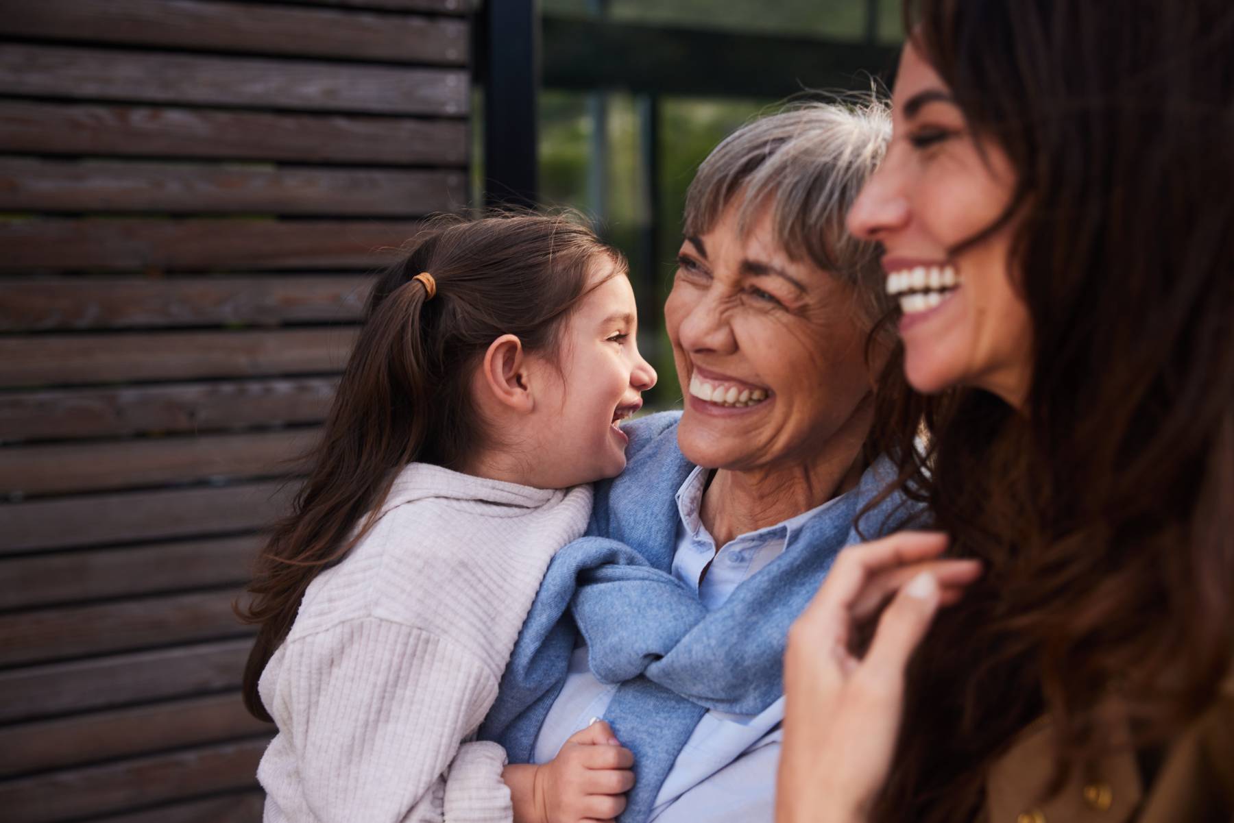A grandmother, mother and daughter hug and laugh together