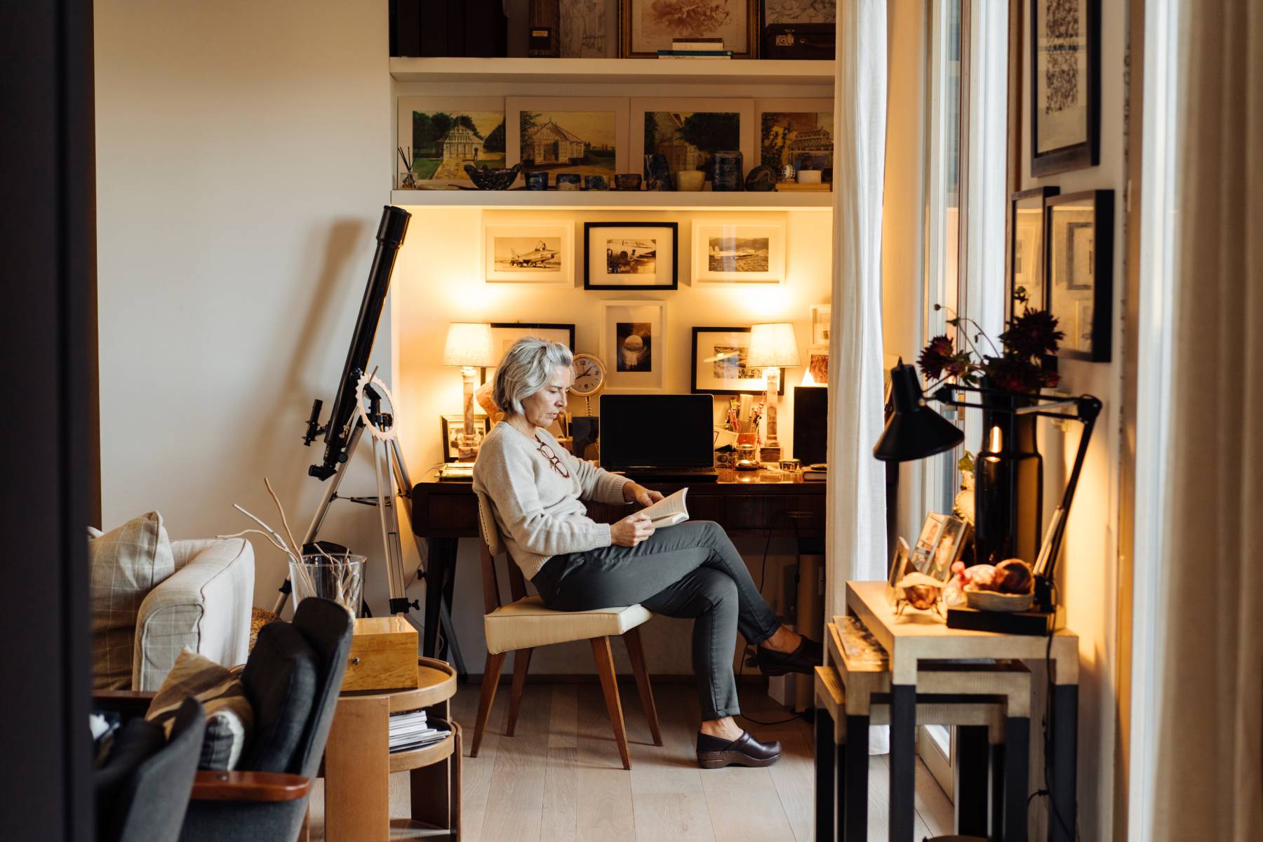A lady reads a book in a study nook of her well furnished home