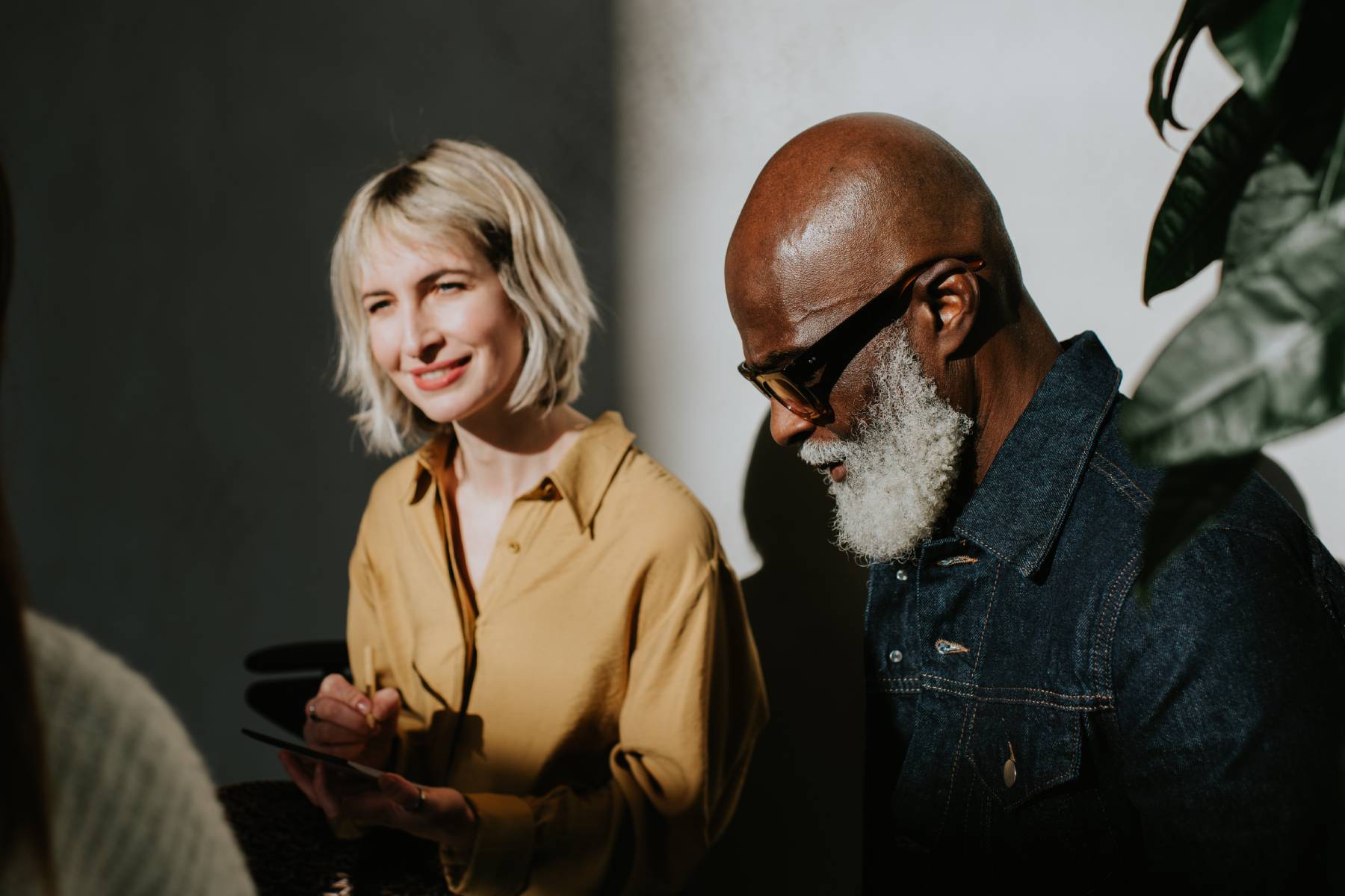 A man and woman study information on a tablet while talking to someone
