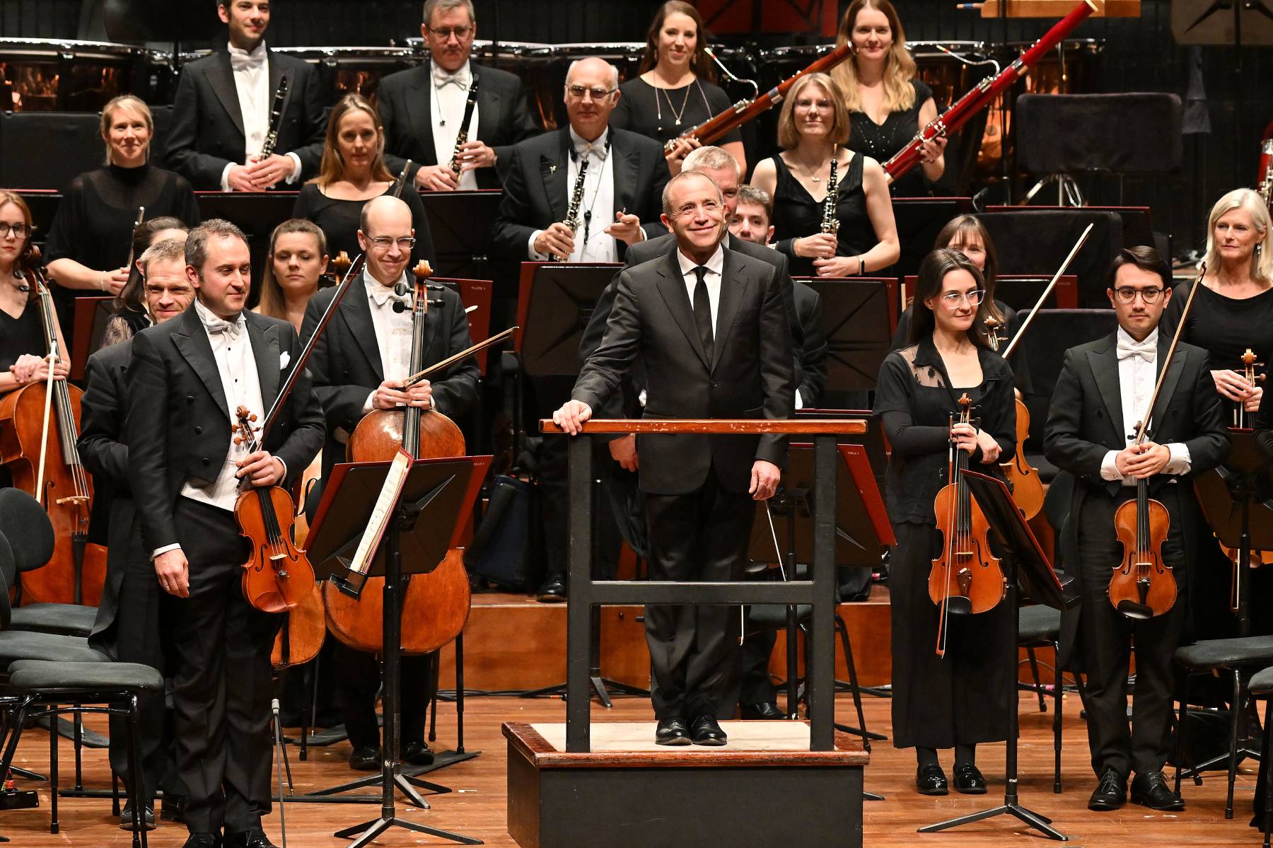 The Bournemouth Symphony Orchestra stands while the audience applauds, with conductor Mark Wigglesworth in front