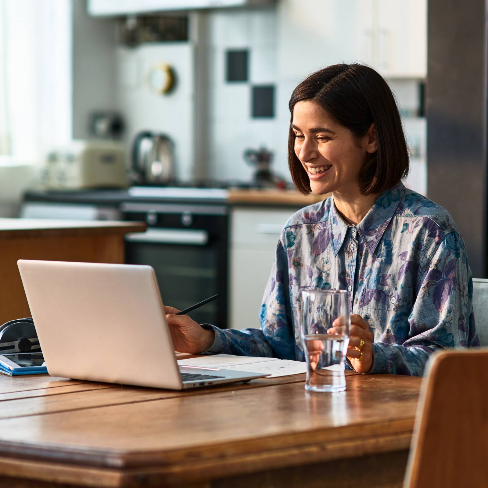 A woman talks on a video call on her laptop while sitting in her kitchen