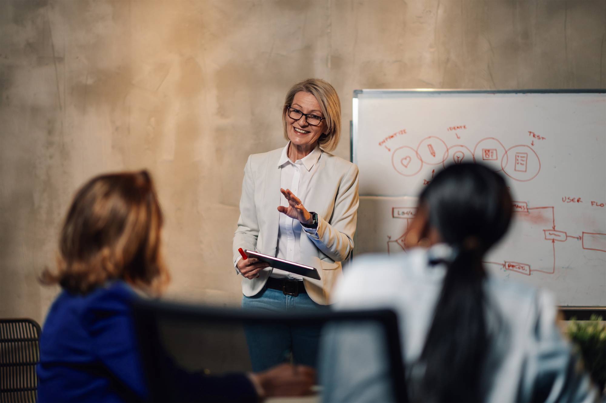 A financial adviser speaks to other advisers while standing by a whiteboard