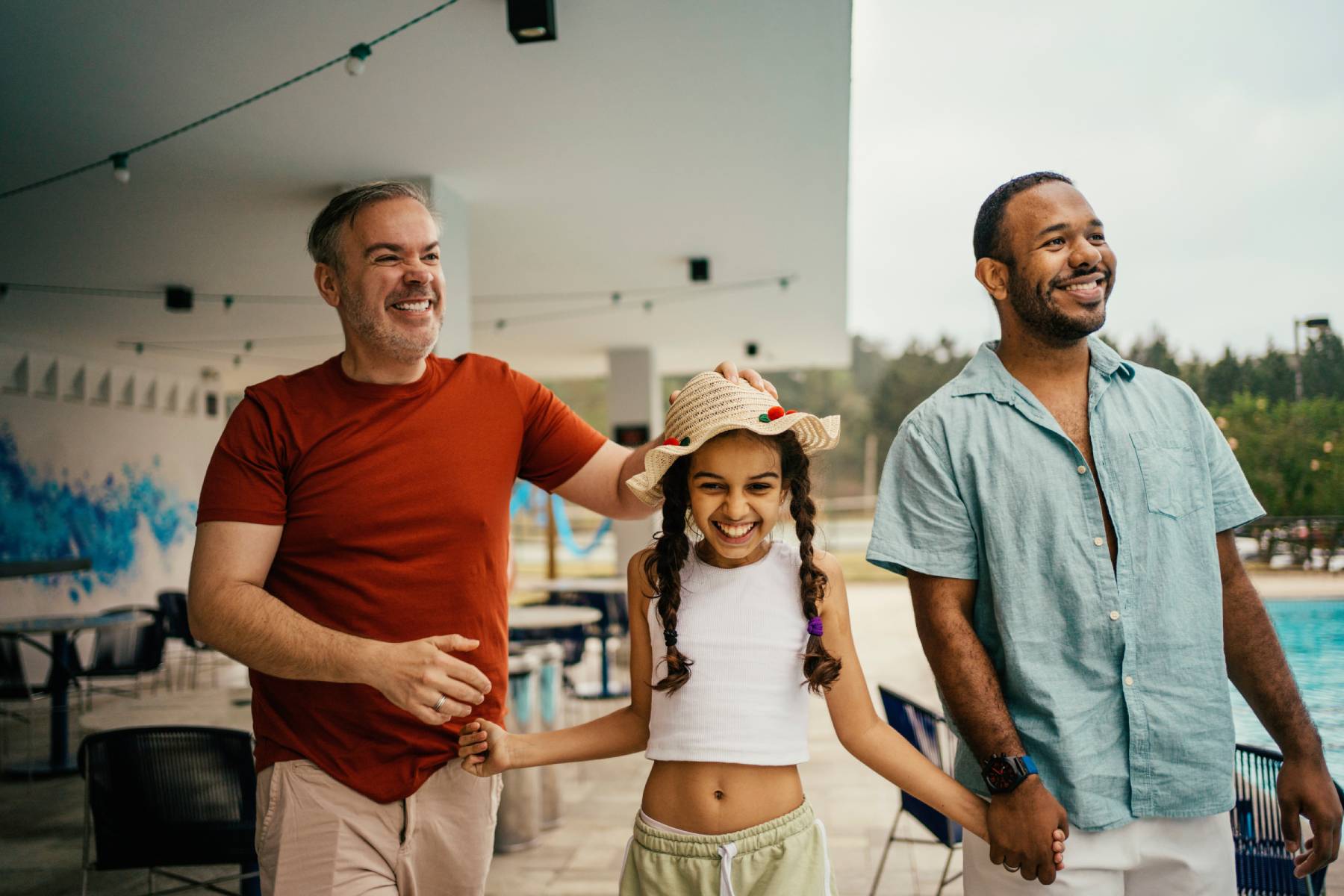 Fathers hold hands with their daughter at a public pool