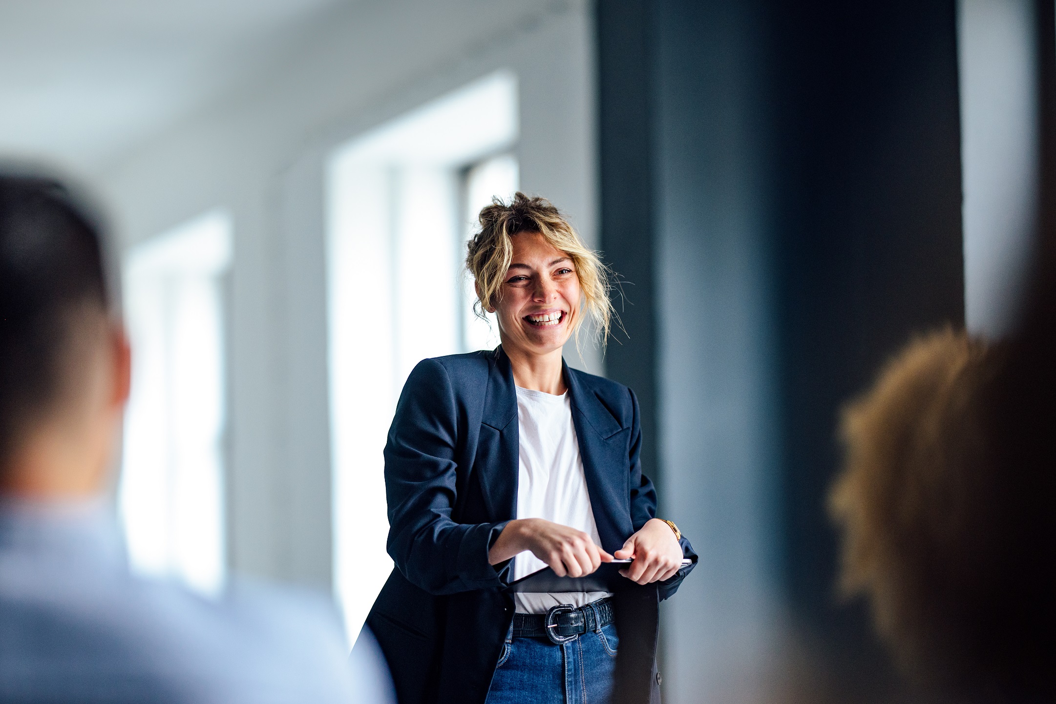 Woman holding an ipad stood up smiling in front of an audience