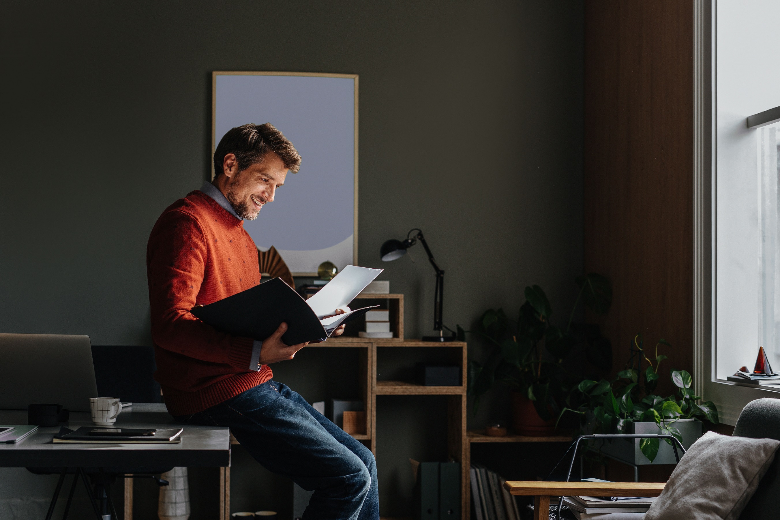 An entrepreneur leans against their desk in an office and reads documents