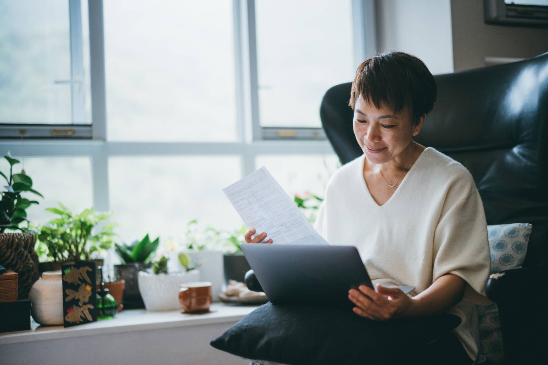 A lady reading a laptop and documents while seated in her home