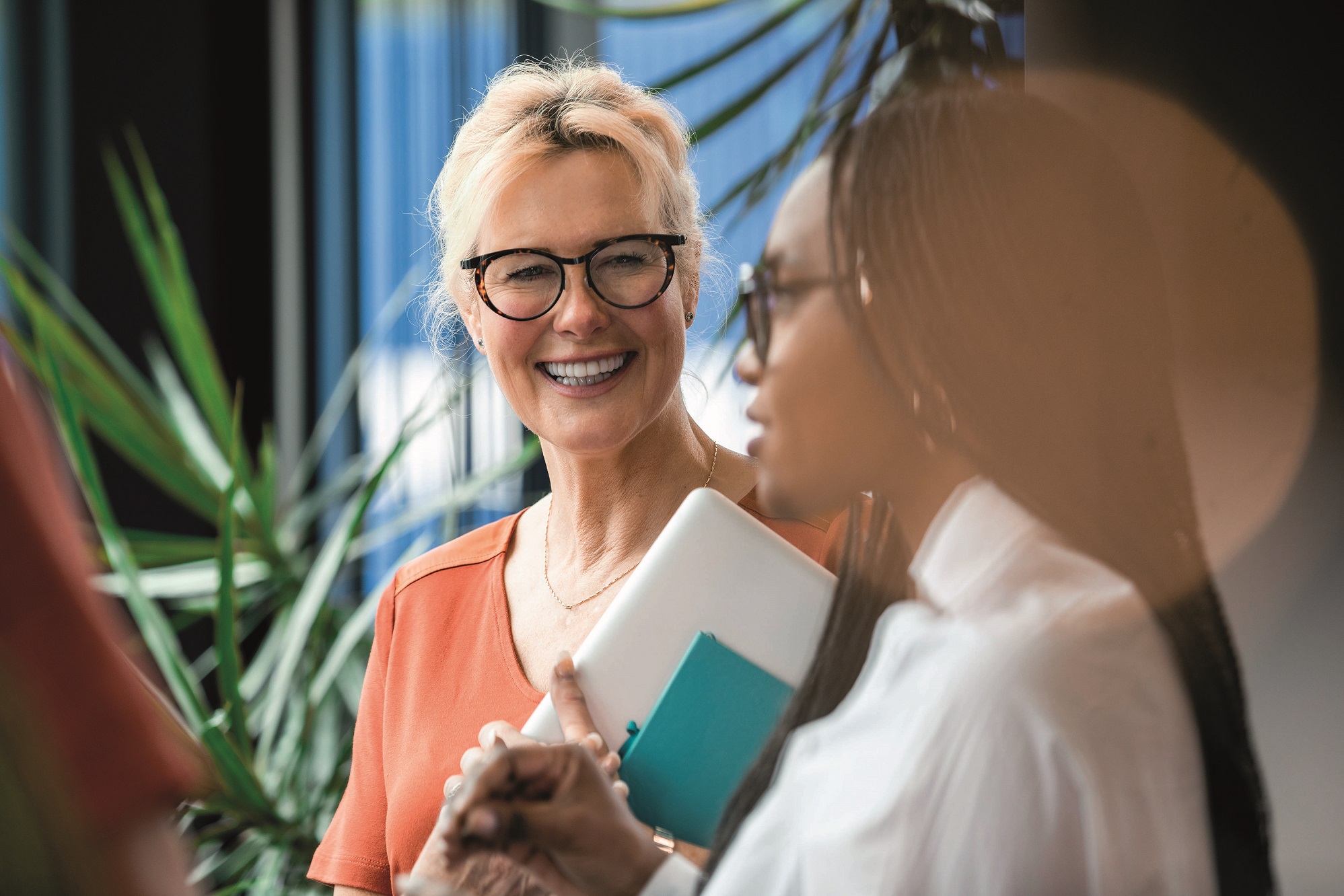 A lady with grey hair wearing black framed glasses, smiling at another lady wearing glasses