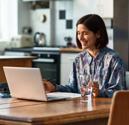 A young woman smiling at her laptop whilst sat at her kitchen table