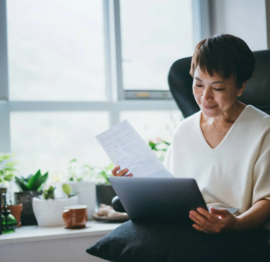 Older aisan lady looking at her tablet and documents sat by a window
