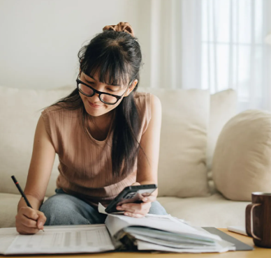 Young woman wearing glasses writing in a notepad on a coffee table