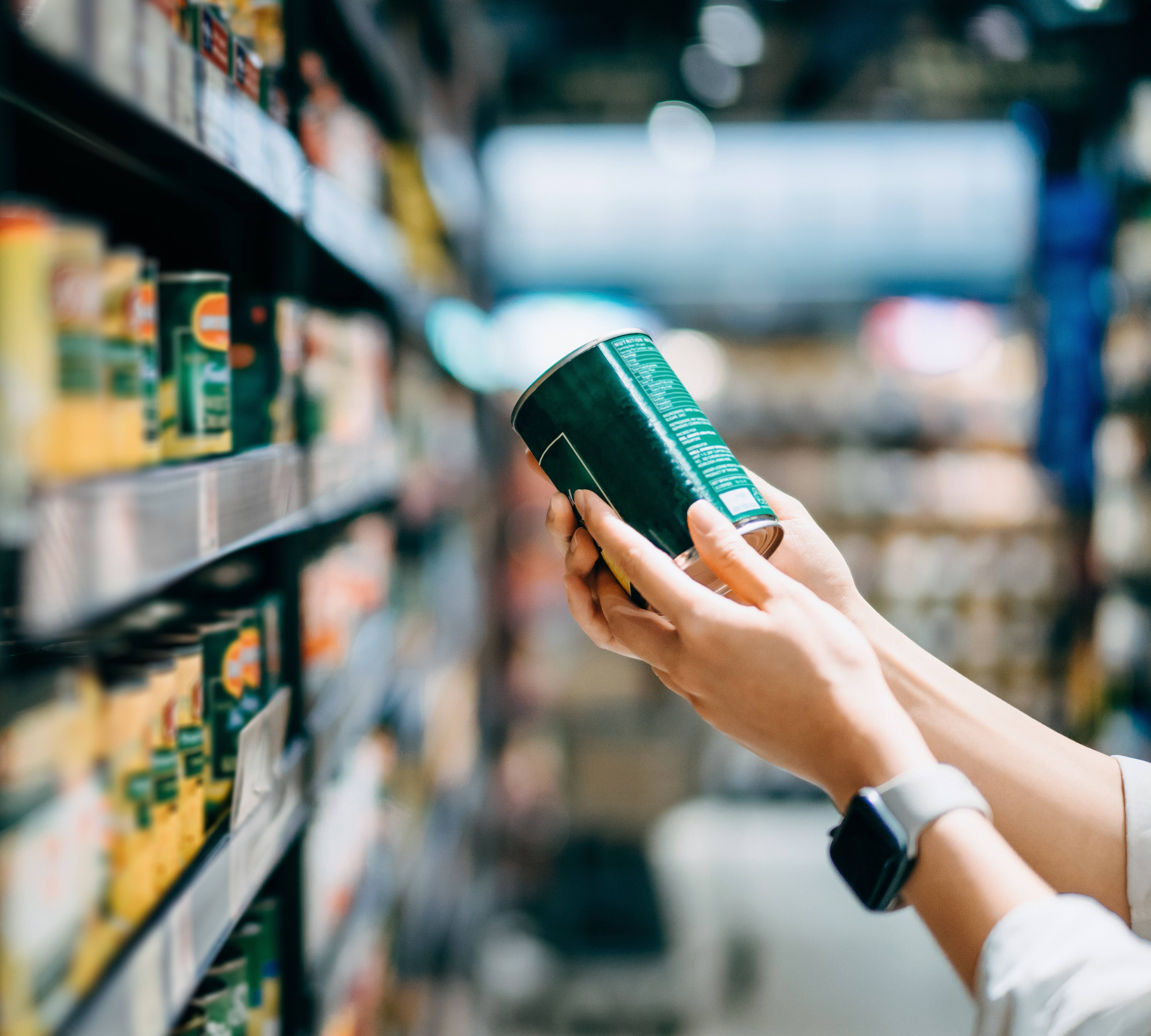 Close up of a woman holding a tin can and grocery shopping in a supermarket