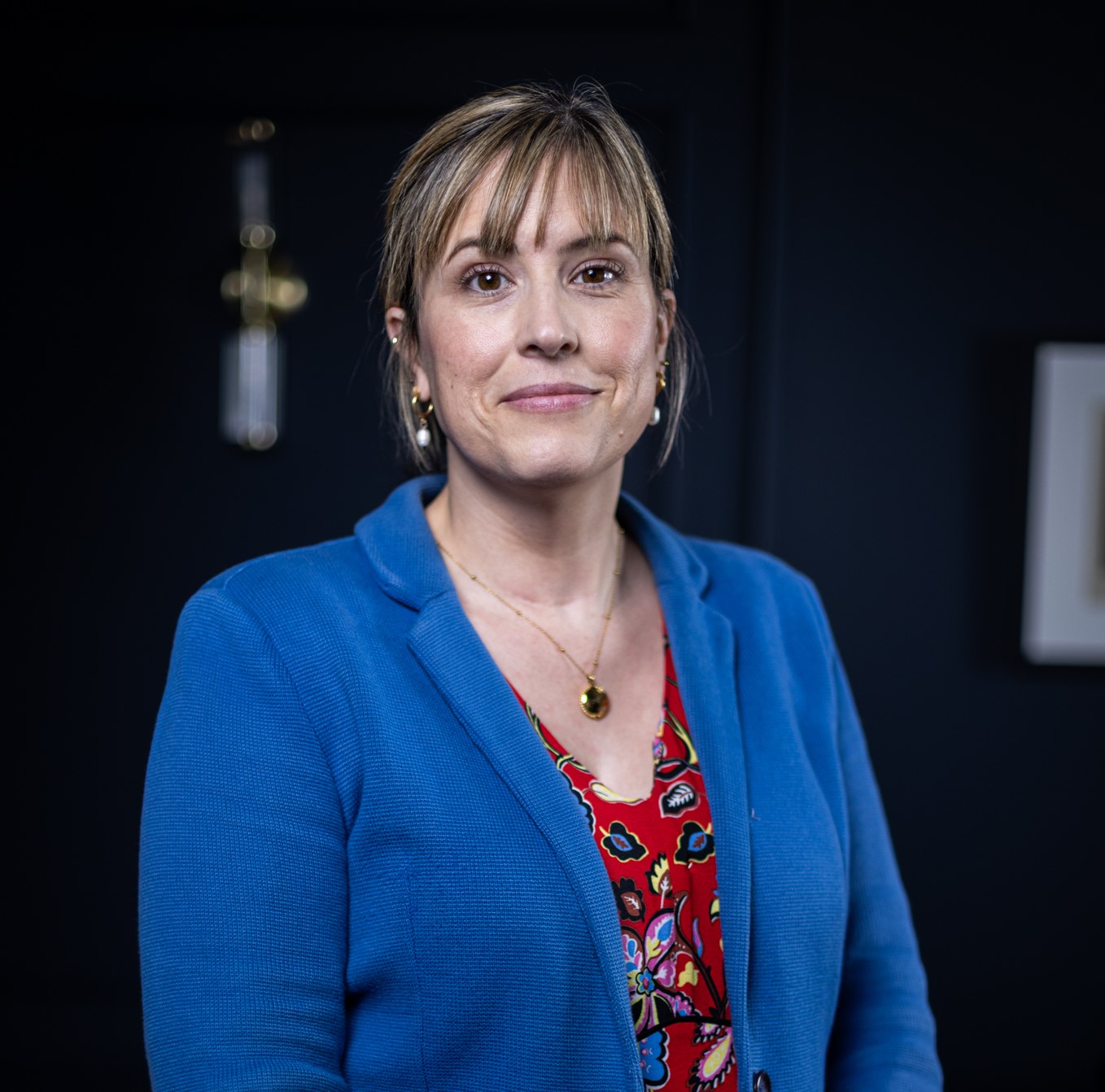 The image shows Rebecca Williams, Financial Planning Divisional Lead at Rathbones, wearing a blue blazer and red dress