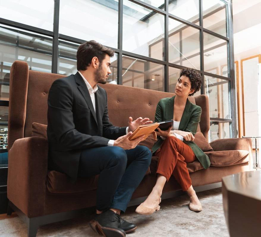 A man and a woman have a discussion on a sofa in a work office
