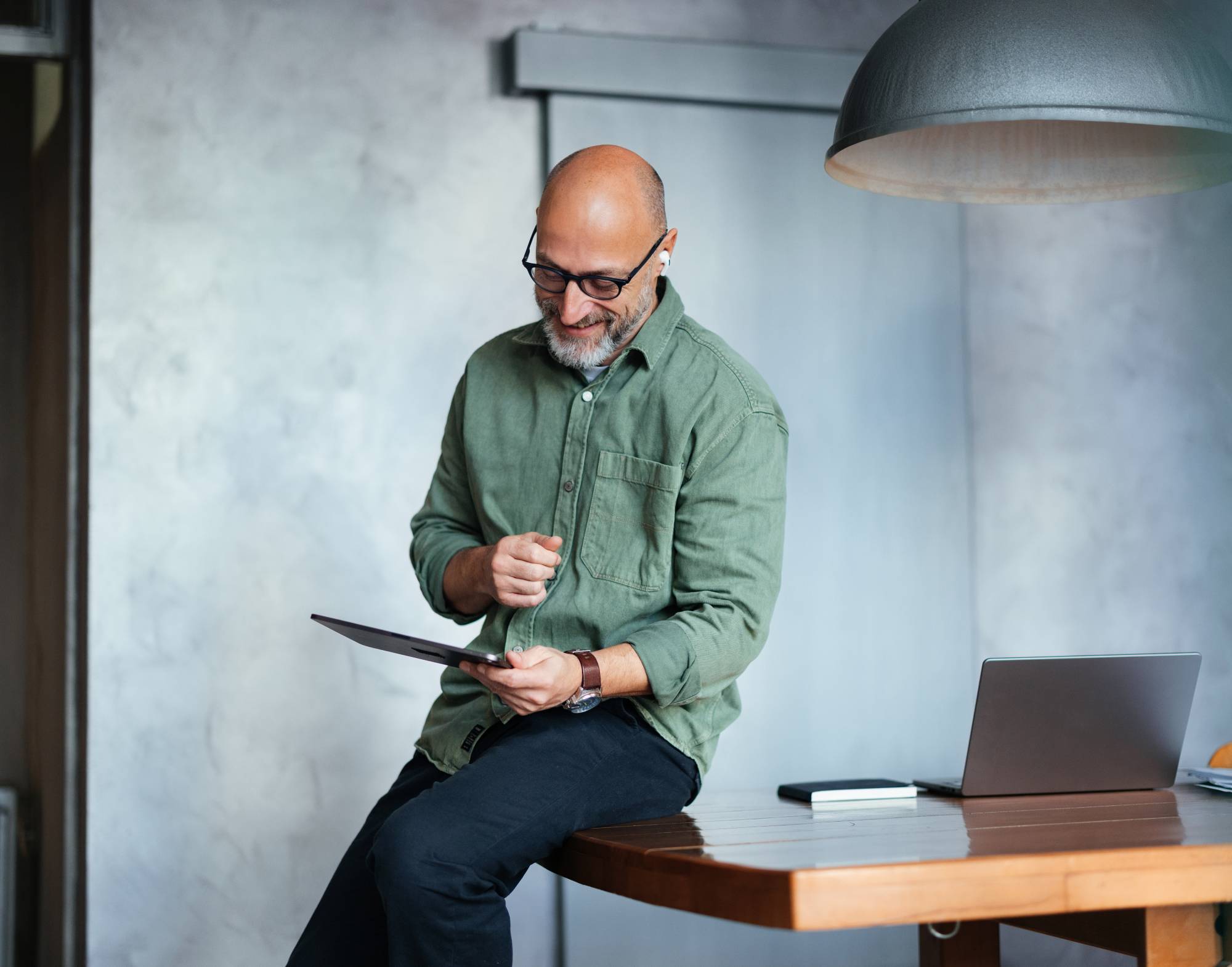 A man leans on his desk while looking at a tablet device