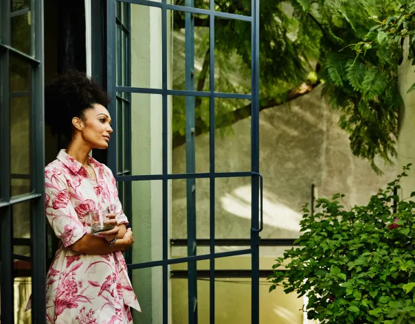 A woman wearing a floral dress looks out the window