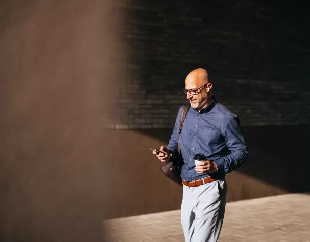 A businessman checks his phone while walking in the sun
