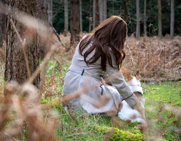 A victim of modern slavery supported by the Justice & Care charity sits with a dog in a wood