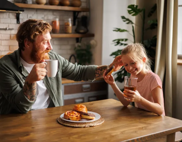 A father and daughter sitting at a kitchen table with drinks and food, representing planning ahead and making time to think about the future and retirement