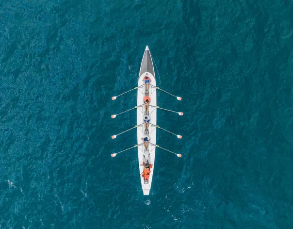 Overhead aerial view of a rowing team in a long narrow boat paddling in sync across deep blue water