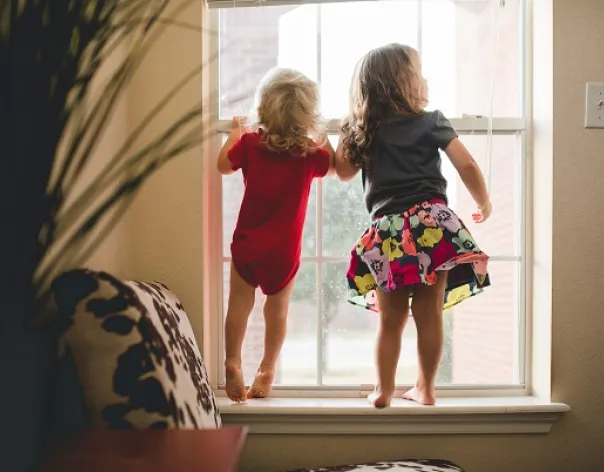 Two children looking out a window in a home