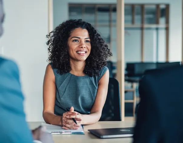A businesswoman sits in a meeting and speaks to colleagues