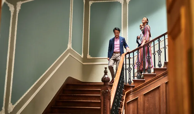 A young couple walk down the stairs of a stately home, behind an estate agent