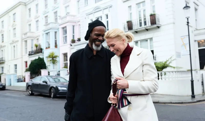 A couple laugh together while walking along a terrace housed street