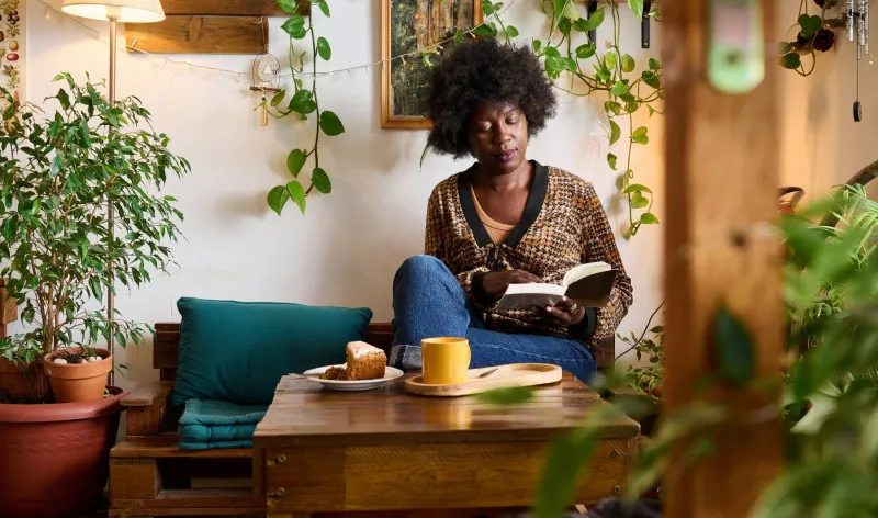 A woman sits in a café reading a book while having a hot drink and cake