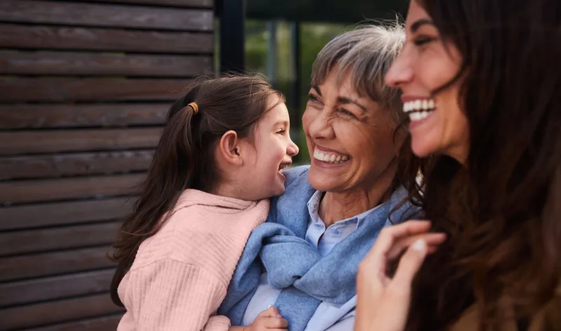 A grandmother holds her daughter while laughing with her daughter