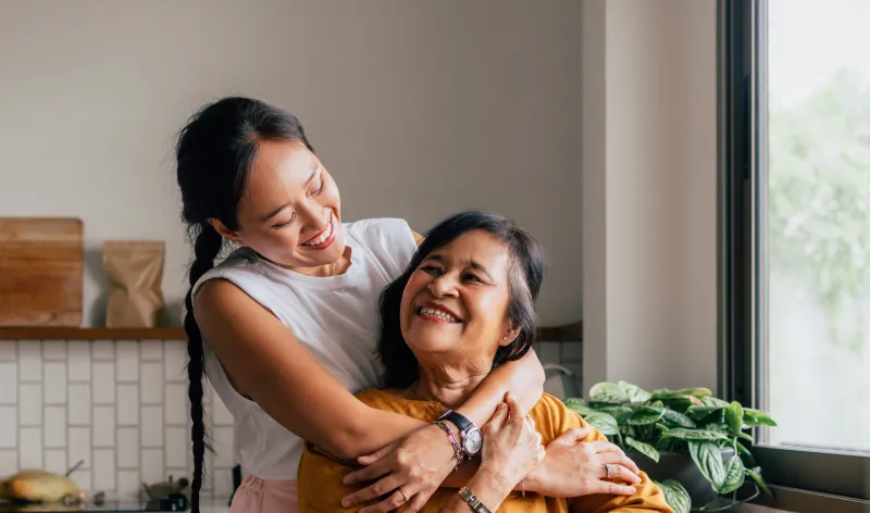 A daughter hugs her mum while they have tea together in their kitchen