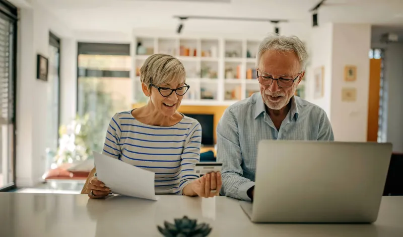 A couple sit together at their kitchen bench and discuss their financial plan together