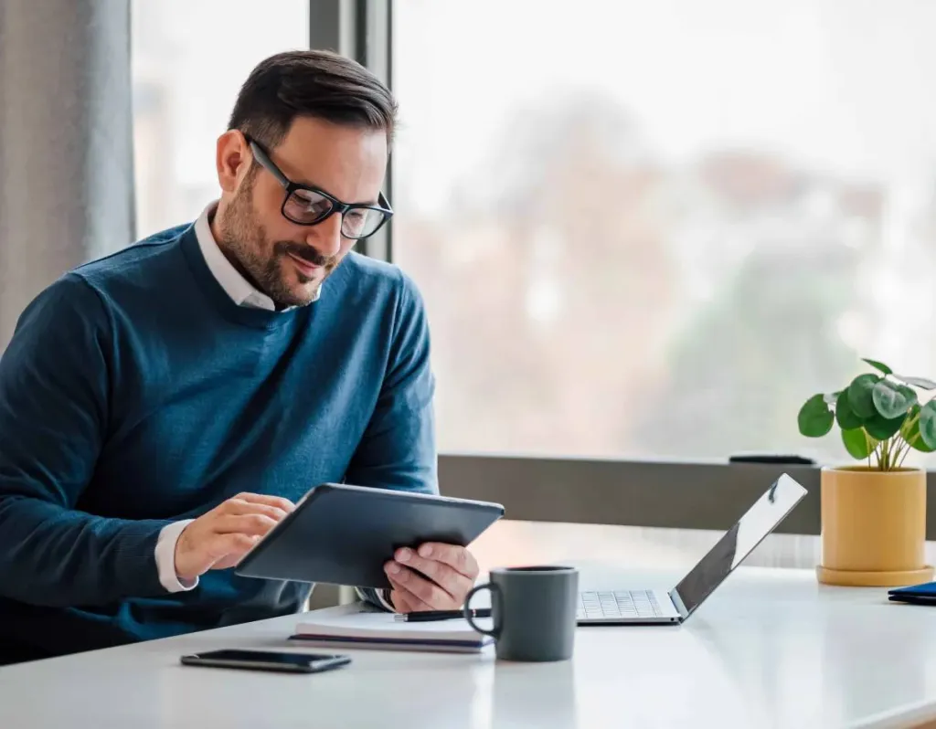 A businessman using a tablet and a laptop at his desk