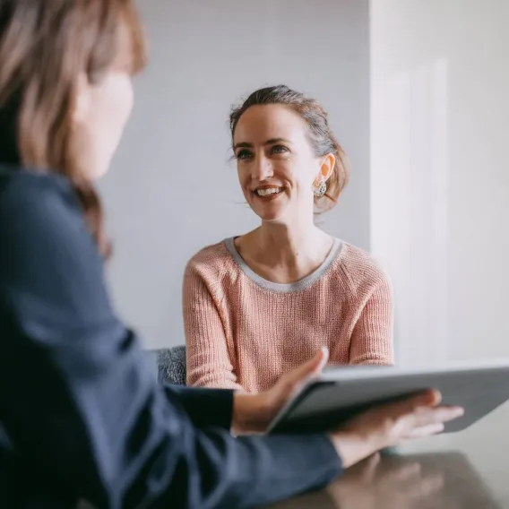 A financial adviser holds a tablet while meeting with their client