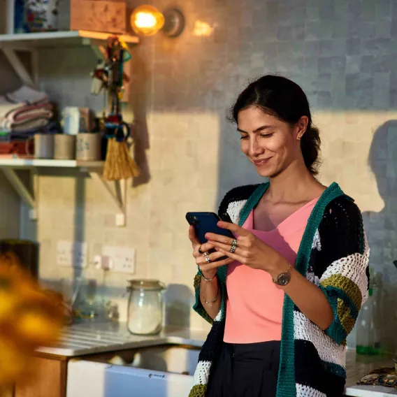 A young woman in her kitchen checks her phone
