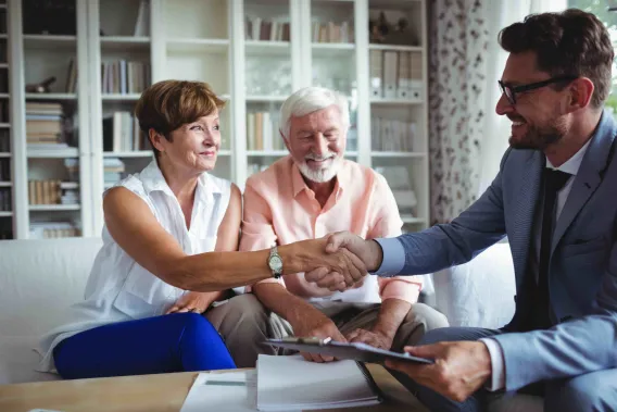 A couple shake hands with their financial adviser during a meeting in their home
