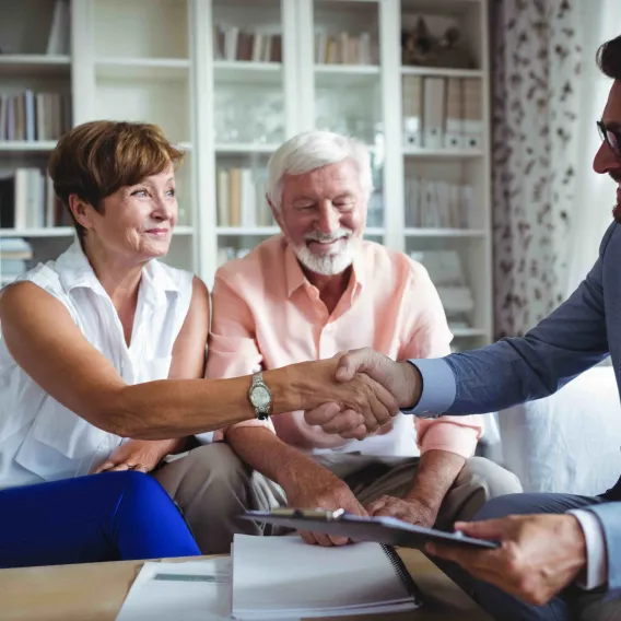 A couple shake hands with their financial adviser during a meeting in their home