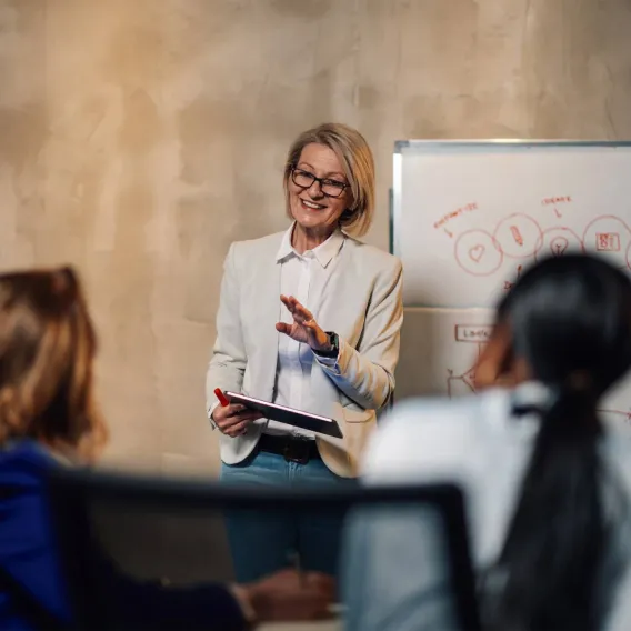 A financial adviser speaks to other advisers while standing by a whiteboard