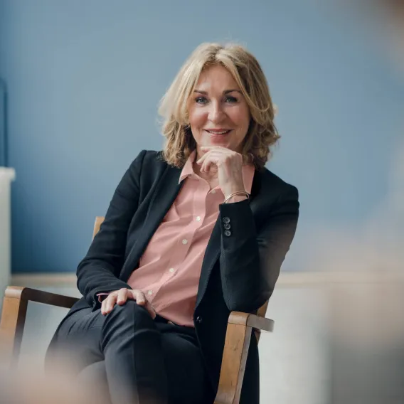 A professional woman looks towards the camera with a curious facial expression while sat in a chair
