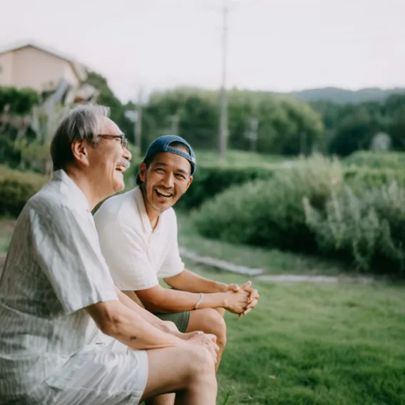 A father and adult son laughing together in a countryside setting