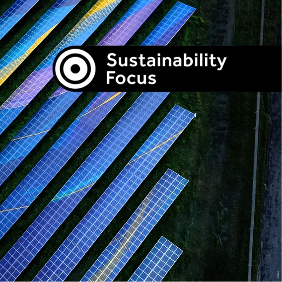 A bird's eye view of a solar farm next to a busy road at dusk, with a "Sustainability Focus" stamp over the top