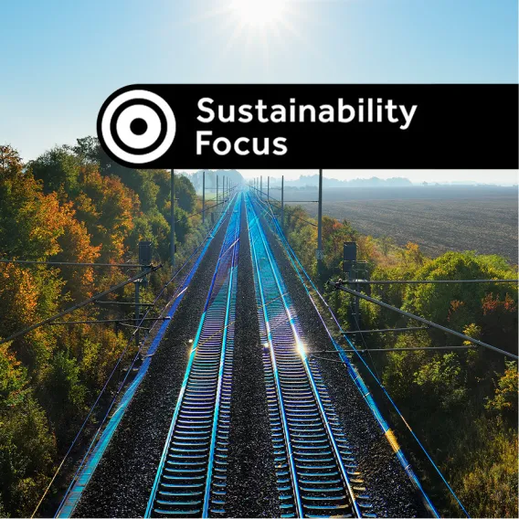 Looking down on sun-drenched train tracks cutting through the countryside, with a "Sustainability Focus" stamp on top