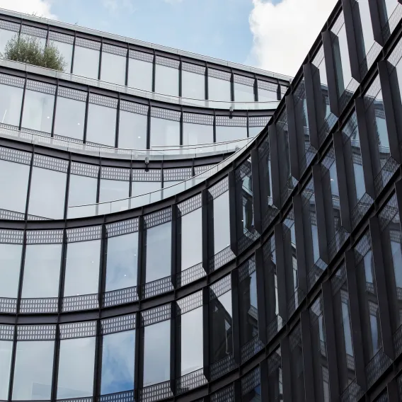 Looking up towards the glass face of a corporate office building with blue sky in the background