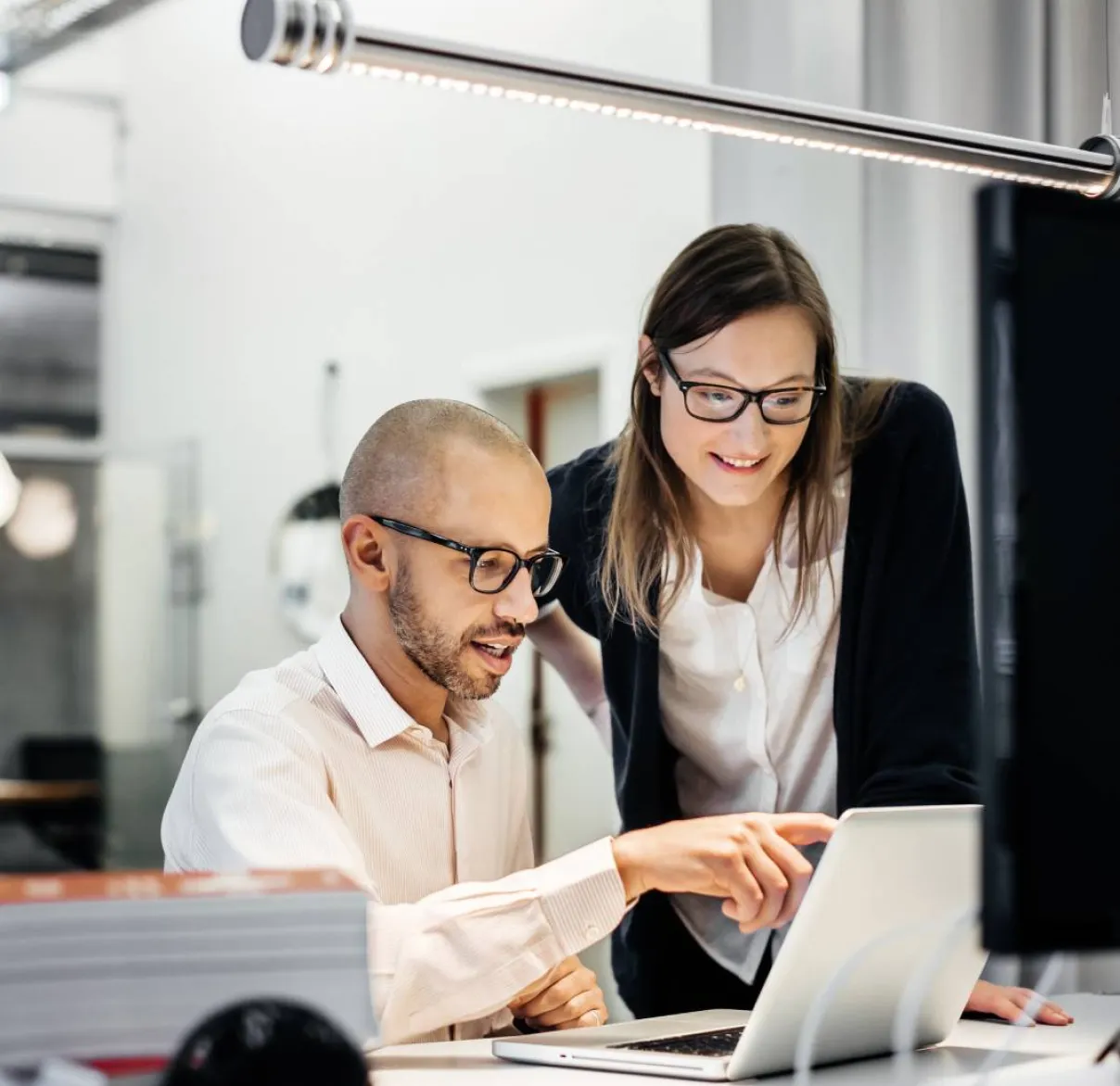 A man and woman in an office look at a laptop together